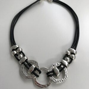 May include: A black leather necklace with three silver rings and silver beads. The rings are textured and have a hammered finish.