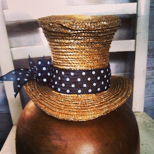 Puede incluir: Un sombrero de paja con una cinta de lunares negros y blancos. El sombrero está sobre una superficie marrón.