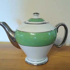 May include: A white teapot with a green band and silver trim. The teapot has a silver spout and handle.