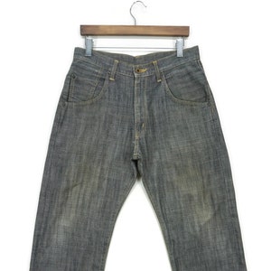 May include: A pair of dark grey denim jeans hanging on a wooden hanger. The jeans have a straight leg and a faded look.