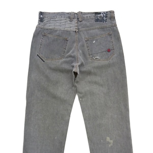 Könnte beinhalten: Graue Jeans aus Denim mit Used-Look und einem kleinen roten und schwarzen Logo auf der Gesäßtasche. Der Bund hat ein schwarzes und weißes, sich wiederholendes Textmuster.