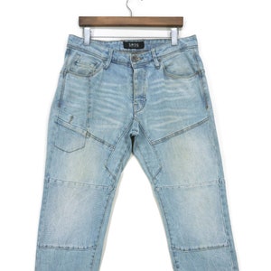 Puede incluir: Vaqueros de mezclilla azul claro con múltiples paneles cosidos y la palabra "SMOG" en la parte posterior de la cintura.