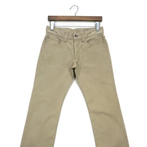 May include: A pair of beige twill pants hanging on a wooden hanger. The pants have a straight leg and a classic five-pocket design.