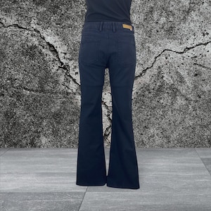 May include: Dark navy blue flared jeans. The jeans have a classic five-pocket design and a small, rectangular tan tag on the back. The pants are shown from the back, with the person wearing them facing away from the camera.