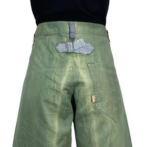 May include: Olive green culottes with a striped fabric detail at the back. The culottes have a relaxed fit and a small pocket on the right side. The fabric appears to be a sturdy cotton or linen blend.