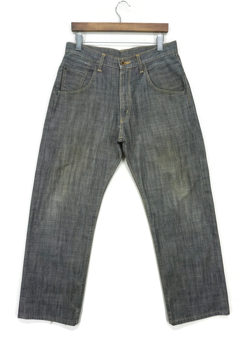 May include: A pair of dark grey denim jeans hanging on a wooden hanger. The jeans have a straight leg and a faded look.