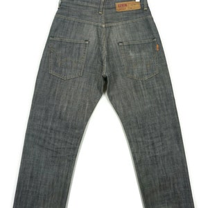 May include: A pair of dark grey denim jeans with a distressed hem. The jeans have a faded look and a small orange tag on the back pocket. The jeans have the word "EDWIN" on a brown label on the back pocket.