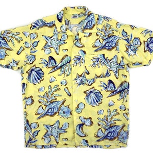 Puede incluir: Una camisa amarilla de manga corta con botones y estampado de conchas marinas azules y marrones.
