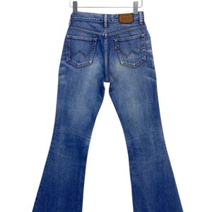 Puede incluir: Un par de pantalones vaqueros azules de mezclilla con una abertura de pierna ancha. Los pantalones vaqueros tienen un parche de cuero marrón en la parte posterior con la palabra "LOWRIN" impresa en él.