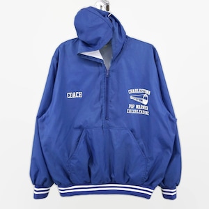 Puede incluir: Chaqueta cortavientos azul con capucha y letras blancas que dicen "Coach" en el lado izquierdo y "Charlestown Pop Warner Cheerleading" con un gráfico de megáfono blanco en el lado derecho. La chaqueta tiene puños a rayas blancas y azules.