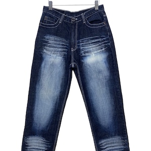Puede incluir: Un par de pantalones vaqueros de mezclilla azul oscuro con detalles de costura clara colgados en una percha de madera.