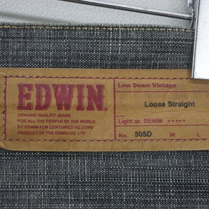 May include: A brown leather label with the text "EDWIN" in red letters. The label also includes the text "Low Down Vintage", "Loose Straight", "Light oz. DENIM", "No. 505D", "W", and "L".
