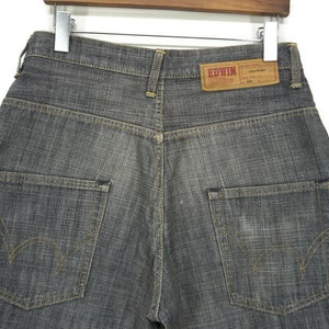 May include: A pair of dark grey denim jeans with a brown leather label that reads "EDWIN" on the back waistband. The jeans have two back pockets with yellow stitching detail.