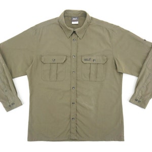 Puede incluir: Una camisa de manga larga de color verde oliva con botones, dos bolsillos en el pecho y una etiqueta de la marca en el bolsillo izquierdo.