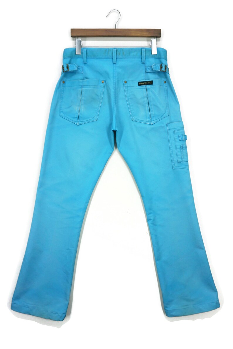 May include: A pair of light blue denim trousers with a cargo pocket on the right leg. The trousers have a belt loop detail and a small black label on the back pocket.