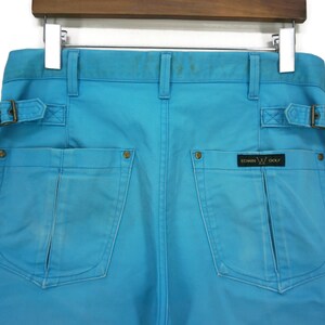 May include: Blue cargo trousers with two large pockets and a belt. The trousers have a gold label that reads "Edwin Golf".