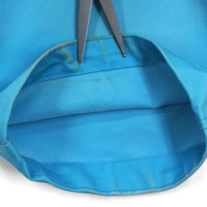 May include: Close-up of the inside of a light blue garment, showing the seam and the fabric. The garment is folded in half and the seam is visible.