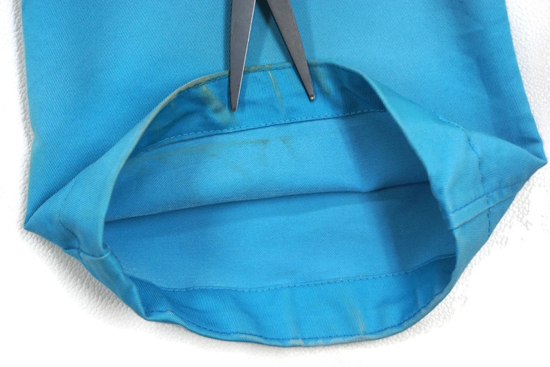 May include: Close-up of the inside of a light blue garment, showing the seam and the fabric. The garment is folded in half and the seam is visible.