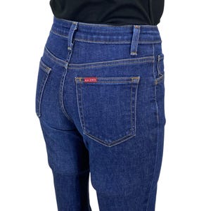 Puede incluir: Vaqueros de mezclilla azul oscuro con cintura alta y diseño clásico de cinco bolsillos. Los vaqueros tienen una pernera recta y una etiqueta roja en el bolsillo trasero. Los vaqueros están hechos de tela de mezclilla duradera.