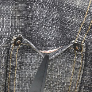 May include: Close-up of a pair of dark blue denim jeans with a textured weave. The jeans have a single back pocket with a button closure and a visible seam running down the side.