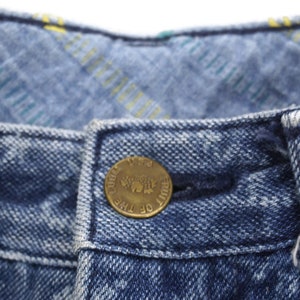 Puede incluir: Primer plano de una cintura de mezclilla azul con un bot&oacute;n de lat&oacute;n que dice "Fruit of the Loom" en un dise&ntilde;o circular.