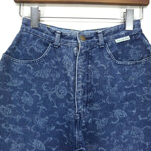 Puede incluir: Vaqueros azules de mezclilla con estampado paisley. Los vaqueros tienen cintura alta y cierre de bot&oacute;n. La etiqueta de los vaqueros dice "Paris of the Lane".