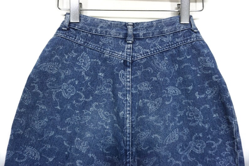 Puede incluir: Un par de pantalones cortos de mezclilla azul con un patr&oacute;n de paisley. Los pantalones cortos tienen cintura alta y cierre de bot&oacute;n.