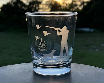 May include: A clear glass tumbler with an etched design of a hunter with a shotgun, a dog, and ducks in flight. The design is in white and is visible against the clear glass.