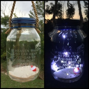 May include: A glass jar with a blue lid and a rope handle. The jar contains sand, a fishing lure, and a message that reads: "If heaven wasn't so far away I'd gas up the boat and be on my way". The jar is lit from within with white LED lights.