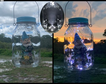 May include: Two glass jars with blue lids and handles, each containing a small gnome figurine and white string lights. The jars are decorated with white deer silhouettes.