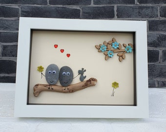 Handmade Pebble Art in White Frame, showing couple with pet dog on driftwood log