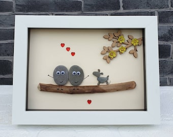 Handmade Pebble Art in White Frame, showing couple with pet dog on driftwood log