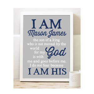 May include: A gray and white framed print with a blue and white text overlay. The text reads "I AM Mason James the son of a king who is not moved by the world for my God is with me and goes before me. I do not fear because I AM HIS."