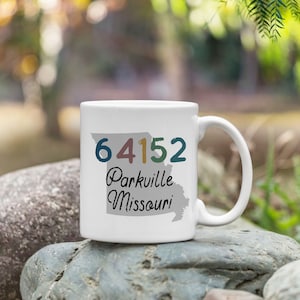 May include: White ceramic coffee mug with a gray outline of the state of Missouri. The mug has the text "64152 Parkville Missouri" printed on it.
