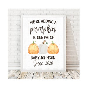 May include: A white sign with the text "We're adding a pumpkin to our patch Baby Johnson June 2020". The sign is decorated with three pumpkins, one white and two orange.