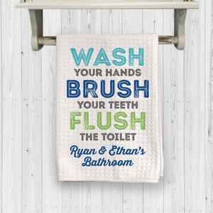 May include: White bathroom hand towel with blue and green text that reads "Wash your hands, Brush your teeth, Flush the toilet, Ryan & Ethan's Bathroom".