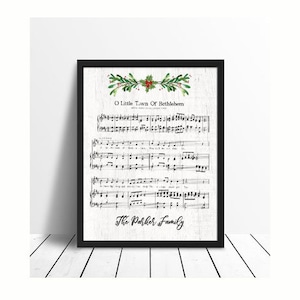 May include: A black framed print with a white background featuring the sheet music for the Christmas carol "O Little Town of Bethlehem". The sheet music is decorated with a green holly sprig with red berries at the top. The print is personalized with the text "The Parker Family".