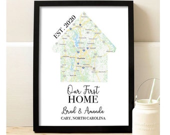 May include: A black framed print with a map of Cary, North Carolina, shaped like a house. The text "EST. 2020" is in the upper left corner. The text "Our First Home Brad & Amanda CARY, NORTH CAROLINA" is below the map.