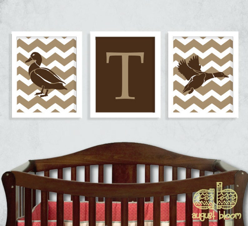 K&ouml;nnte beinhalten: Drei gerahmte Drucke mit einem braunen Chevron-Muster als Hintergrund. Der linke Druck zeigt eine braune Silhouette einer Ente. Der mittlere Druck zeigt einen braunen Buchstaben T. Der rechte Druck zeigt eine braune Silhouette einer Ente im Flug.