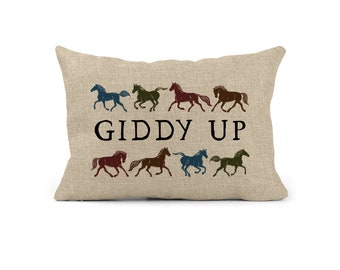 May include: A rectangular beige pillow with a horse theme. The pillow features eight running horse silhouettes in various colors above the words "GIDDY UP" in black. The pillow has a textured appearance.