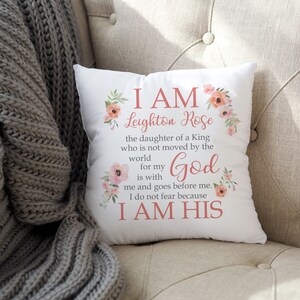 May include: White throw pillow with pink floral design and the text "I AM Leighton Rose the daughter of a King who is not moved by the world for my God is with me and goes before me. I do not fear because I AM HIS"