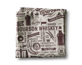 May include: A folded, square, waffle-weave kitchen towel with a repeating pattern of bourbon whiskey-themed graphics in brown and white. The design includes bottles, barrels, and text such as "Bourbon Whiskey" and "Aged for 10 Years."