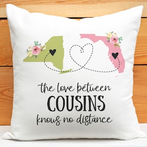 May include: White throw pillow with a green outline of New York and a pink outline of Florida. The outlines are connected by a dotted line with a heart in the middle. The text "the love between COUSINS knows no distance" is printed below the outlines.