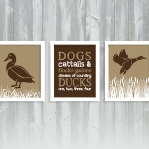 May include: Three framed prints with duck-themed art. The prints feature brown ducks in various poses against a tan background, with white grass accents. One print has text that reads "DOGS cattails & flocks galore dreams of counting DUCKS one, two, three, four."