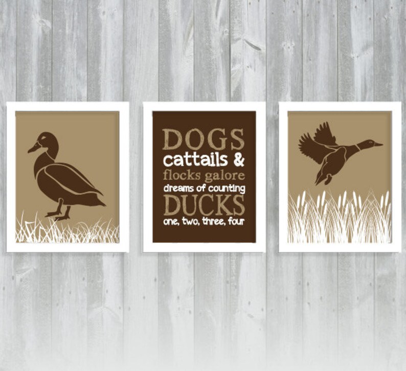 May include: Three framed prints with duck-themed art. The prints feature brown ducks in various poses against a tan background, with white grass accents. One print has text that reads "DOGS cattails & flocks galore dreams of counting DUCKS one, two, three, four."