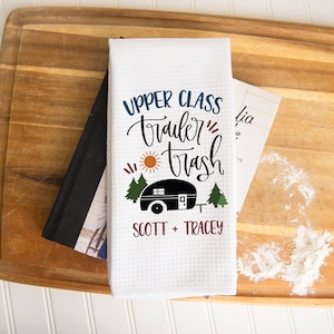 May include: White kitchen towel with a black and white illustration of a camper and the text "Upper Class Trailer Trash" with the names "Scott + Tracey" below.