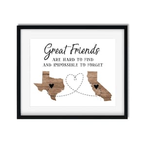 May include: A black framed print with a white background and the text "Great Friends are hard to find and impossible to forget". The print features a stylized outline of Texas and California with a heart connecting the two states.