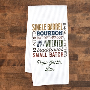 May include: White kitchen towel with a brown, blue, green, and red design that says "Single Barrel Bourbon Barrel-Proof High Wheated Rye Traditional Small Batch Papa Jack's Bar".