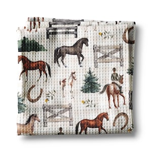 May include: White waffle-weave fabric with a repeating pattern of horses, fences, horseshoes, and riders. The horses are various shades of brown and black, with green trees and yellow flowers scattered throughout the design.