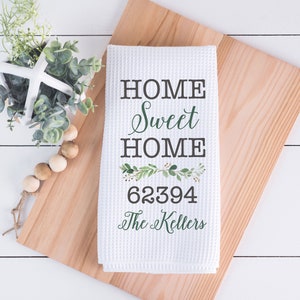 May include: White kitchen towel with the text "Home Sweet Home" in black lettering, a green floral design, and the text "62394 The  Kellers" in black lettering.
